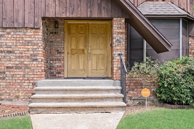 view of exterior entry with roof with shingles and brick siding