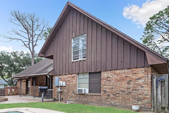 exterior space featuring a shingled roof, a patio, cooling unit, board and batten siding, and brick siding