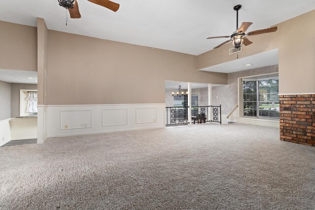 unfurnished living room featuring a wainscoted wall, carpet floors, ceiling fan with notable chandelier, and visible vents