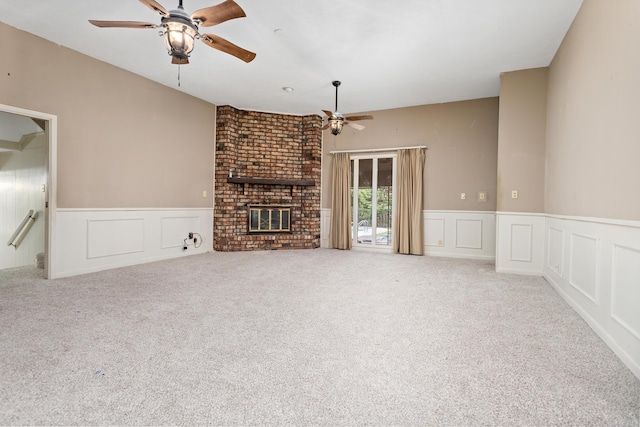 unfurnished living room featuring ceiling fan, a wainscoted wall, carpet, and a fireplace