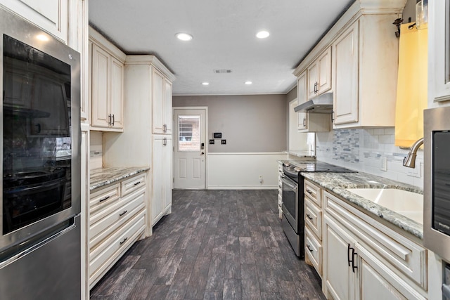 kitchen with light stone counters, under cabinet range hood, tasteful backsplash, dark wood finished floors, and stainless steel range with electric stovetop