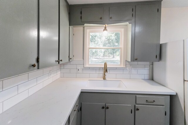 kitchen featuring gray cabinetry, white fridge, sink, and tasteful backsplash