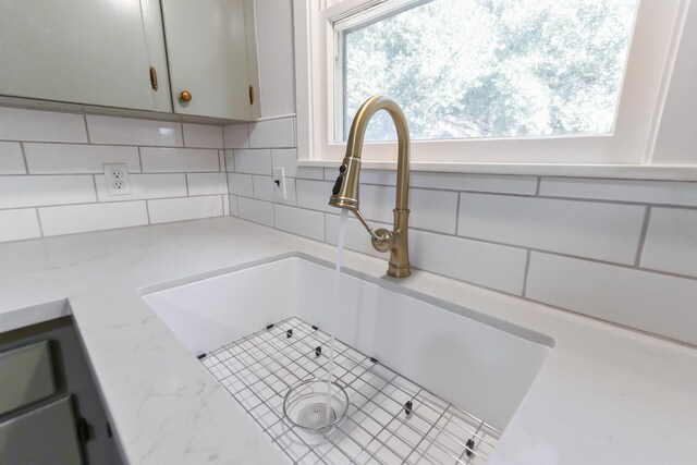 room details with light stone counters, white cabinetry, sink, and tasteful backsplash