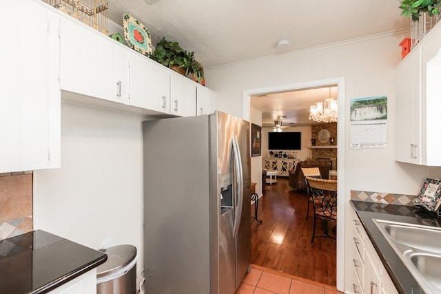 kitchen with dark countertops, white cabinets, stainless steel fridge with ice dispenser, and a sink