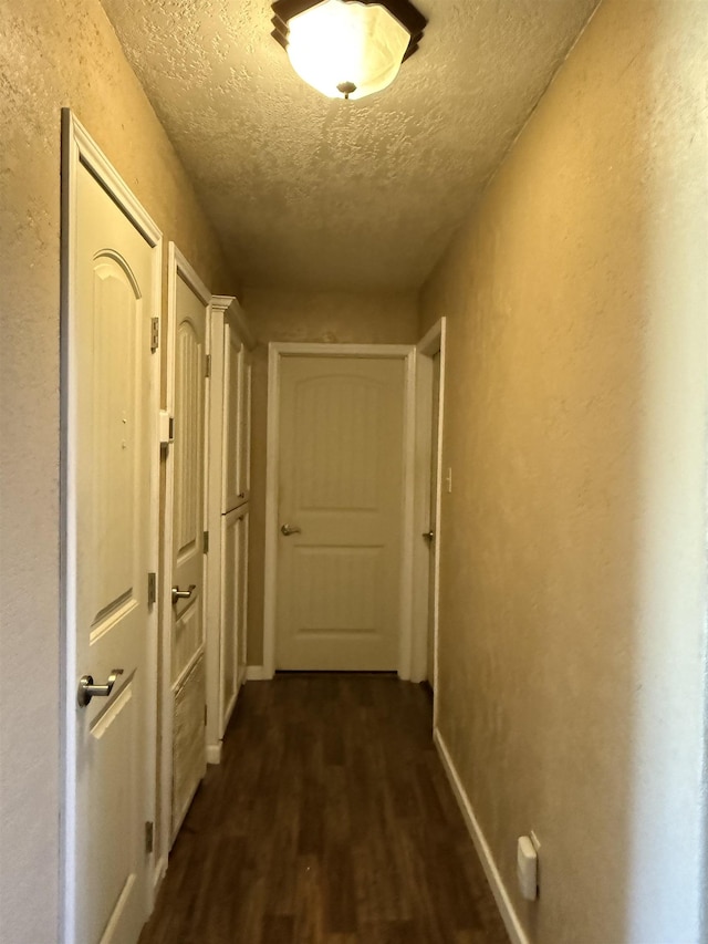 hallway with baseboards, a textured ceiling, dark wood-style flooring, and a textured wall