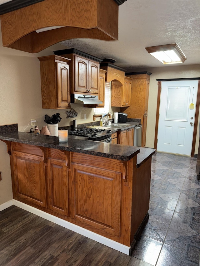 kitchen with under cabinet range hood, a kitchen breakfast bar, gas stove, a peninsula, and brown cabinetry