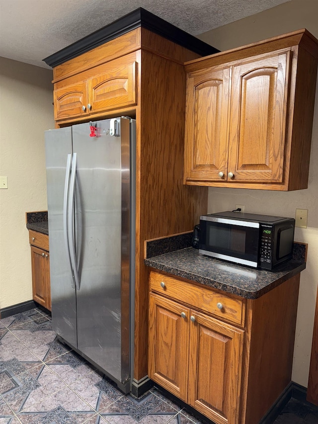 kitchen with brown cabinetry, a textured ceiling, freestanding refrigerator, and black microwave