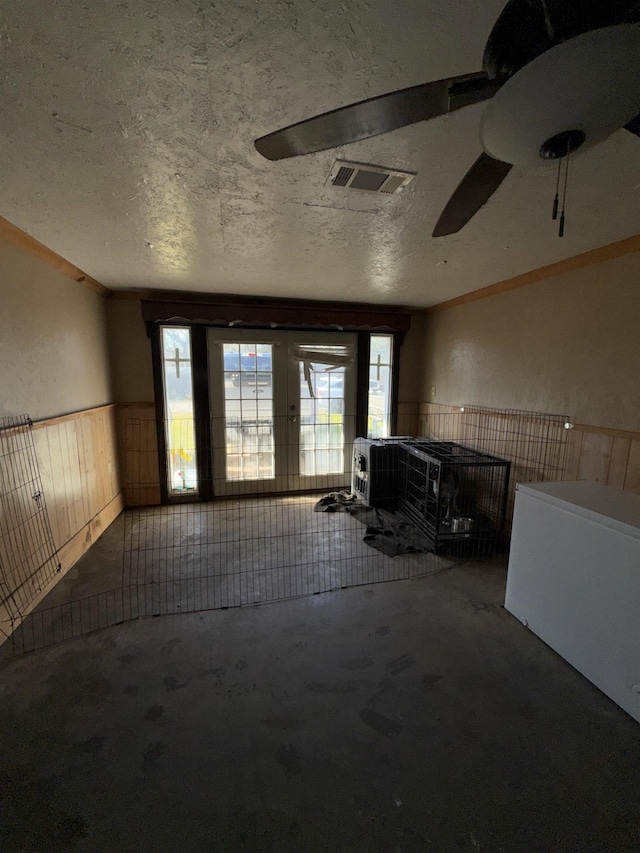 misc room featuring a textured ceiling, unfinished concrete floors, a healthy amount of sunlight, and wainscoting