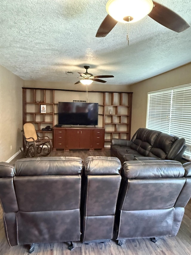 living room featuring wood finished floors, a ceiling fan, baseboards, and a textured ceiling