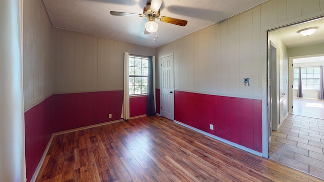 empty room with wood walls, ceiling fan, dark hardwood / wood-style floors, and a wealth of natural light