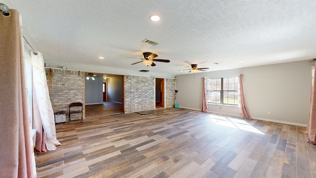 empty room with wood-type flooring, a textured ceiling, ceiling fan, and brick wall