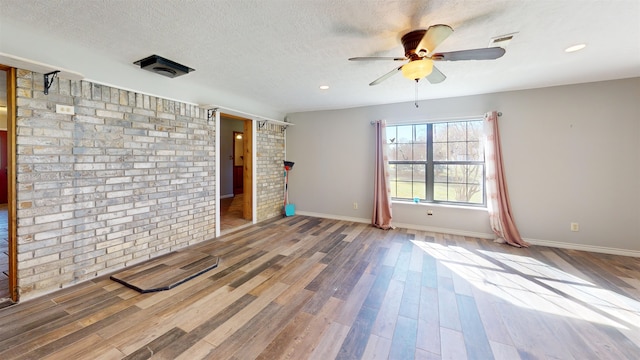 spare room with a textured ceiling, hardwood / wood-style flooring, ceiling fan, and brick wall