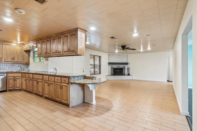 kitchen featuring light stone countertops, ceiling fan, stainless steel dishwasher, backsplash, and a fireplace