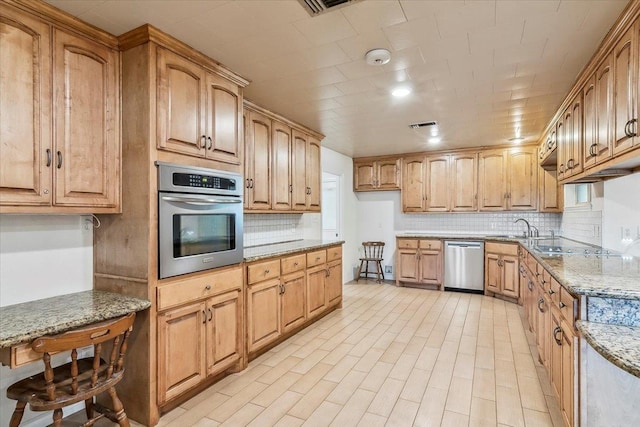 kitchen with tasteful backsplash, light stone counters, sink, and appliances with stainless steel finishes