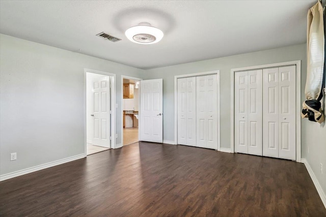 unfurnished bedroom featuring two closets and dark wood-type flooring