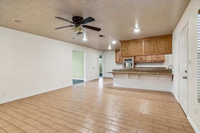 kitchen with ceiling fan, a kitchen breakfast bar, kitchen peninsula, dark stone countertops, and oven