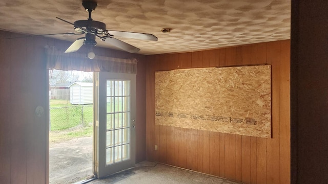 doorway with wooden walls and a ceiling fan