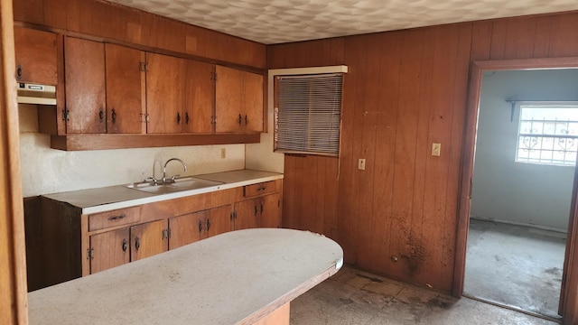 kitchen with brown cabinetry, wood walls, light countertops, and a sink