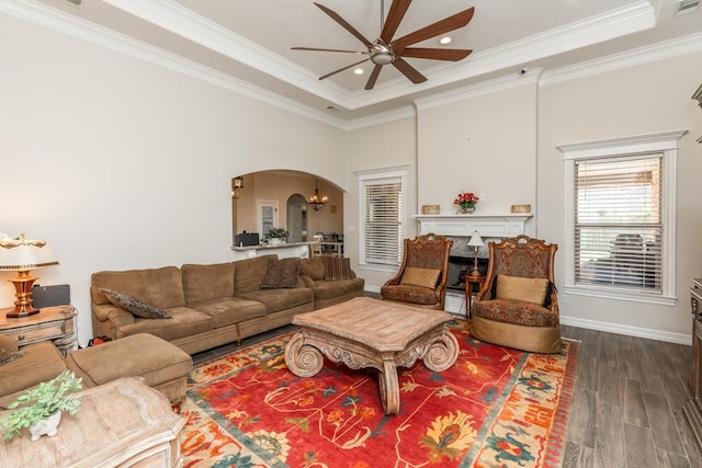 living room featuring ornamental molding, ceiling fan with notable chandelier, a tray ceiling, and dark wood-type flooring