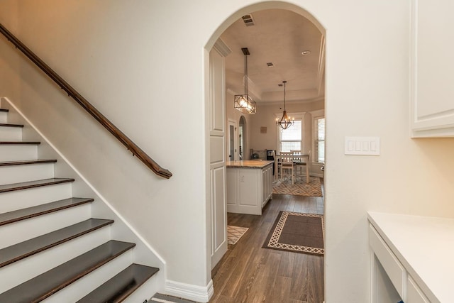 staircase with a chandelier, wood-type flooring, and a tray ceiling