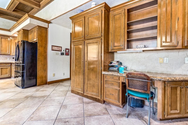 kitchen featuring coffered ceiling, black refrigerator, built in desk, ornamental molding, and light tile patterned floors