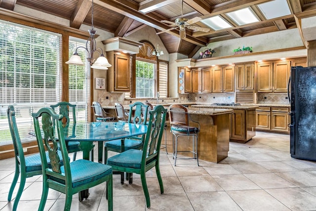 kitchen featuring light stone countertops, tasteful backsplash, pendant lighting, black refrigerator, and a kitchen island