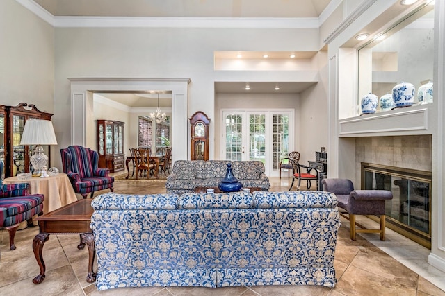 living room featuring a tiled fireplace, a towering ceiling, ornamental molding, and a notable chandelier