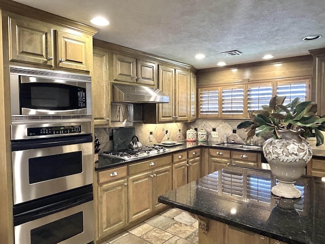 kitchen featuring sink, backsplash, dark stone counters, a textured ceiling, and appliances with stainless steel finishes