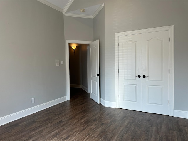 unfurnished bedroom with dark wood-type flooring, crown molding, a high ceiling, and a closet