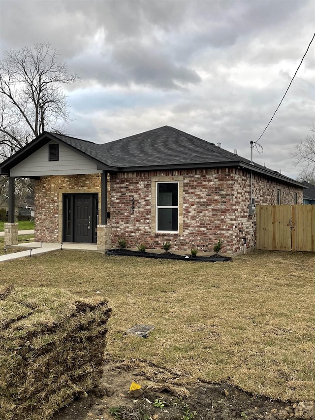 back of property featuring brick siding, a yard, fence, and roof with shingles