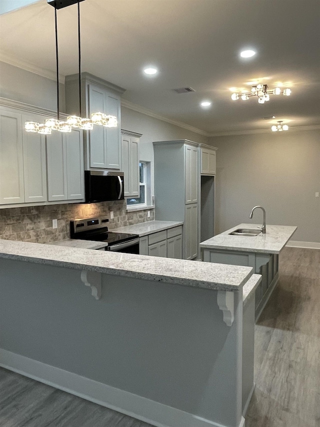 kitchen with ornamental molding, a peninsula, a kitchen island with sink, stainless steel appliances, and a sink