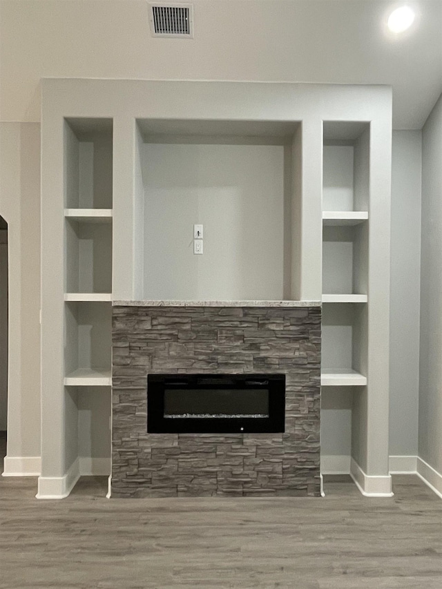 details with baseboards, visible vents, a glass covered fireplace, wood finished floors, and built in shelves