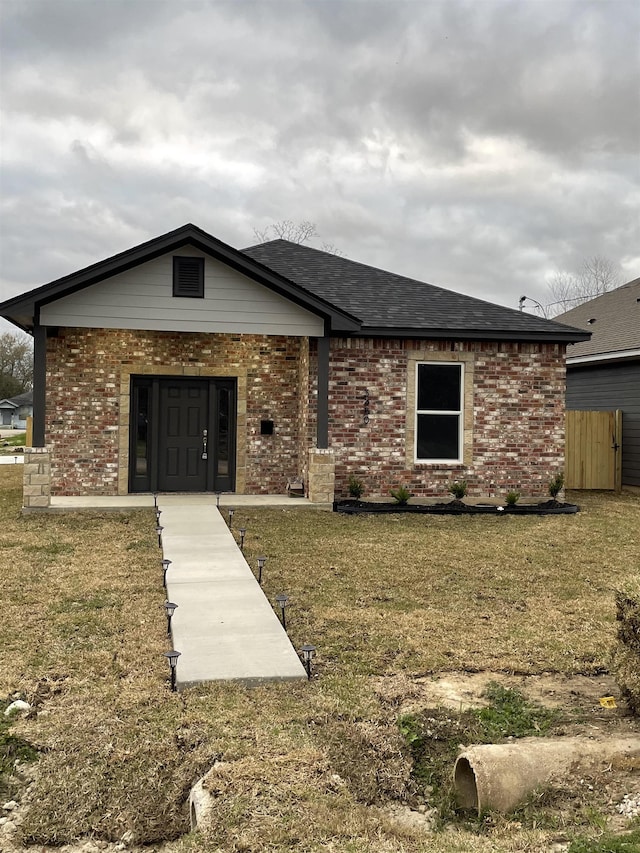 view of front of home featuring a shingled roof, a front yard, and brick siding