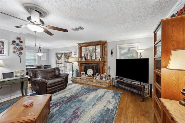 living area with a ceiling fan, visible vents, crown molding, a brick fireplace, and wood finished floors