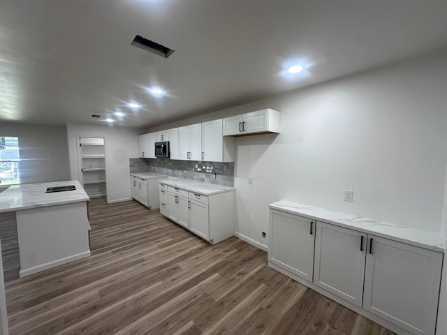 1117 W Dr, Port Neches, TX 77651 - kitchen with stainless steel microwave, white cabinets, wood finished floors, backsplash, and light stone countertops