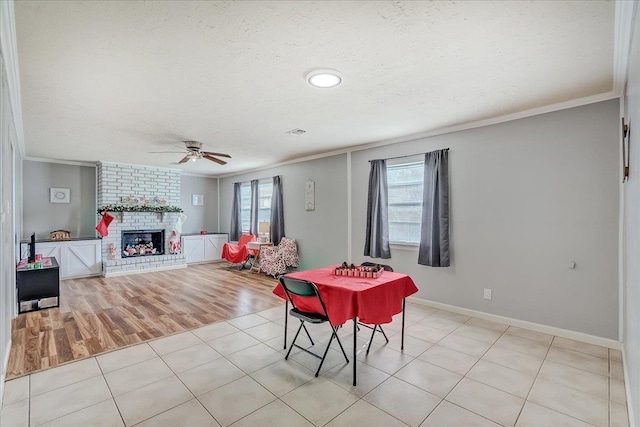 dining area with a brick fireplace, ceiling fan, light tile patterned flooring, and ornamental molding