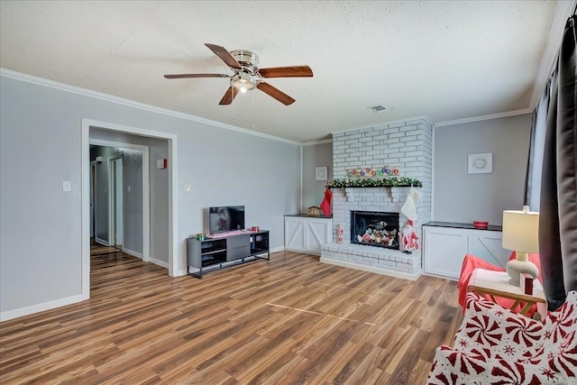 living room featuring hardwood / wood-style flooring, ceiling fan, ornamental molding, a fireplace, and a textured ceiling