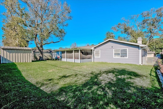 back of property featuring a sunroom, a storage unit, and a lawn