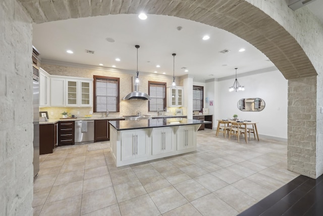 kitchen with wall chimney range hood, tasteful backsplash, glass insert cabinets, a center island, and dishwasher