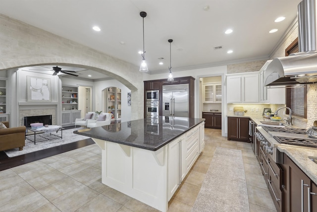 kitchen featuring dark stone counters, built in appliances, ceiling fan, a sink, and open floor plan