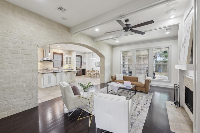living room featuring beamed ceiling, visible vents, ceiling fan, arched walkways, and light wood finished floors