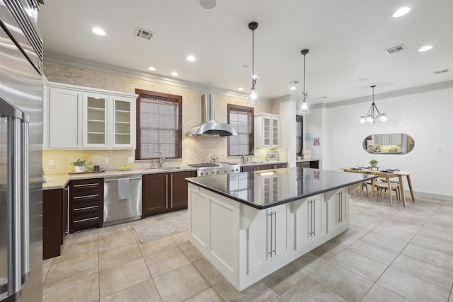 kitchen featuring visible vents, stainless steel appliances, wall chimney range hood, and a sink