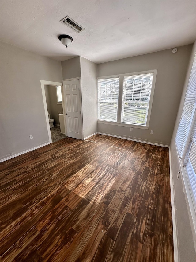 unfurnished bedroom featuring ensuite bath and dark wood-type flooring