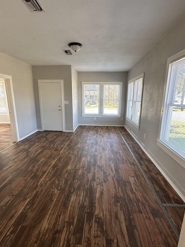 unfurnished living room with a textured ceiling, plenty of natural light, and dark wood-type flooring