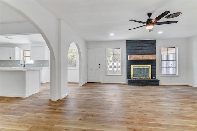 unfurnished living room featuring light hardwood / wood-style flooring, a brick fireplace, ceiling fan, and sink