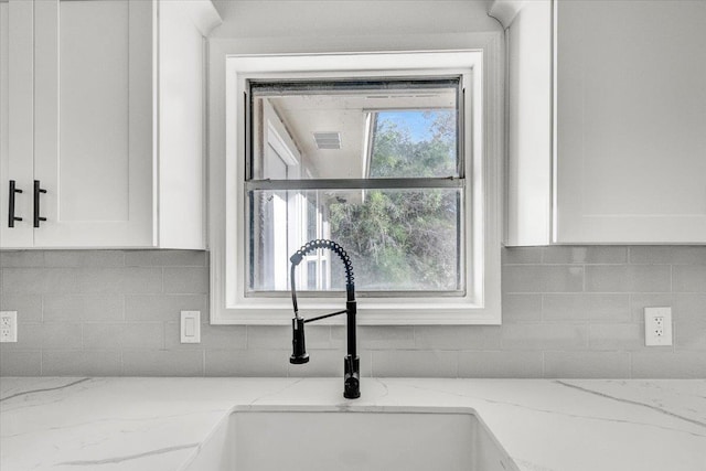 details featuring white cabinetry, decorative backsplash, light stone countertops, and sink