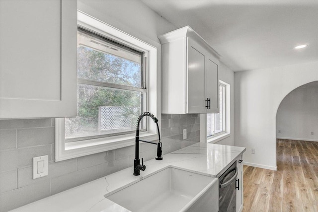 kitchen with light stone countertops, sink, stainless steel dishwasher, decorative backsplash, and white cabinets