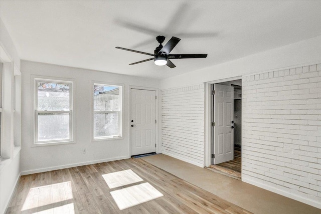 empty room with ceiling fan, light hardwood / wood-style floors, and brick wall