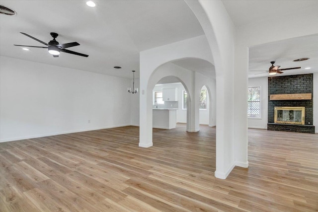 unfurnished living room with a fireplace, ceiling fan with notable chandelier, and light hardwood / wood-style flooring