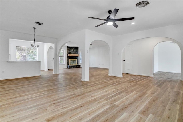 unfurnished living room with ceiling fan with notable chandelier, a large fireplace, and light wood-type flooring